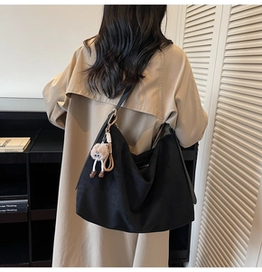 Détail d'un grand sac bandoulière en daim noir avec un pendentif en peluche sur la lanière
