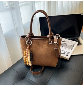Detail of brown suede bucket bag with colorful beaded charm and adjustable strap
