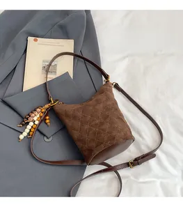 Gros plan sur un sac seau en daim matelassé marron avec breloque en perles de bois