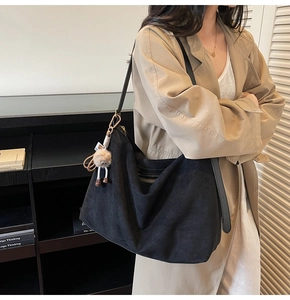 Détail du sac hobo en daim noir avec large bandoulière en cuir et breloque en peluche