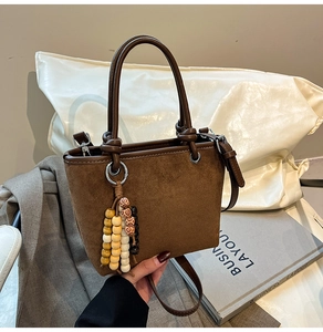 Detail of dark brown faux suede bucket bag with decorative beaded tassel and double handles