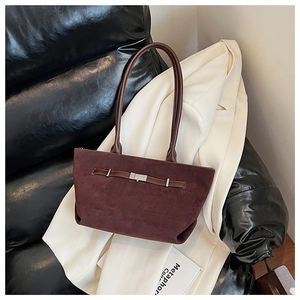 Detail of dark burgundy suede tote bag with slim straps on a beige blazer and leather sofa