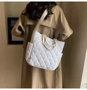 Detail of white quilted tote bag with side pocket and adjustable strap worn by a model