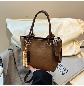 Detail of brown faux suede bucket bag with wooden bead charm and leather handles