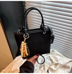 Detail of black suede bucket bag featuring colorful wooden bead tassel and double handles