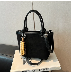 Detail of black matte suede bucket bag featuring ethnic wood bead charm and silver hardware