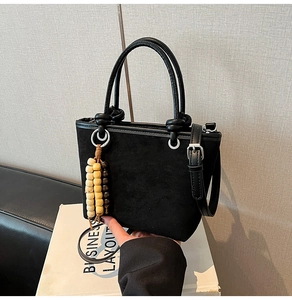 Detail of black suede bucket bag featuring cylindrical handles and vintage wooden beads