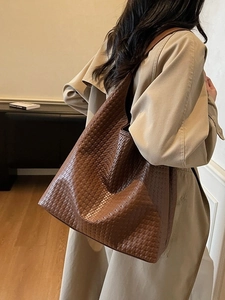 Brown woven leather tote bag shown from a back view on a model in a trench coat