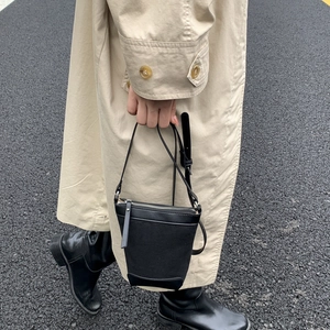 Detail of black canvas and leather crossbody bucket bag on a minimalist beige trench coat