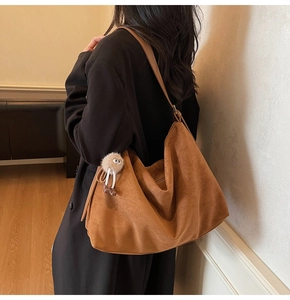 Sac hobo en daim marron avec charm peluche blanche porté à l'épaule