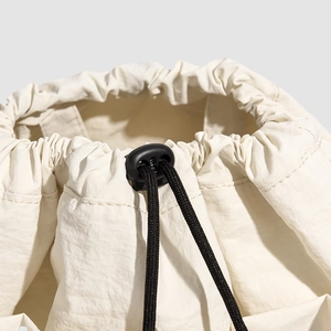 Detail of cream drawstring closure with black cord lock on textured nylon backpack