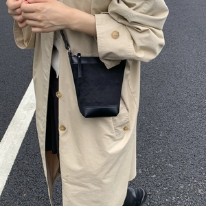 Detail of a black matte bucket bag with a zip closure worn with a stylish trench coat