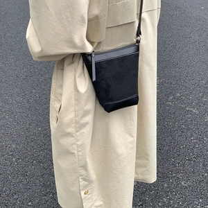 Detail of a black textured bucket bag with matte suede panels and adjustable slim strap