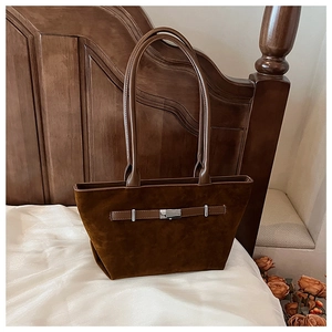 Detail of a brown suede tote bag featuring a leather strap and silver metal buckle accent