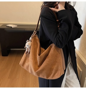 Détail d'un grand sac hobo en daim marron avec un charm en peluche sur la bandoulière