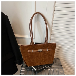 Detail of dark brown suede tote bag with metal buckle on a metallic suitcase