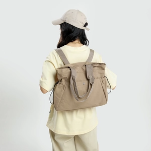 Detail of khaki water-resistant tote backpack showing drawstring side pockets and snap button
