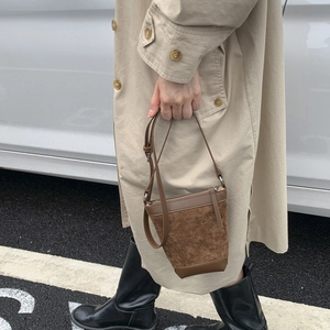 Detail of brown suede bucket bag with contrast leather trim and zipper closure