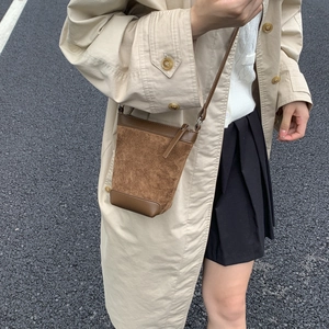 Detail shot of a vintage brown matte bucket bag worn over a beige autumn trench coat
