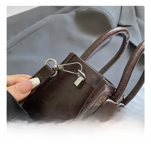 Detail showing the premium silver metal hook and thick handle on a dark brown handbag