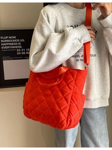 Bright orange-red large quilted tote bag with adjustable strap worn by a model
