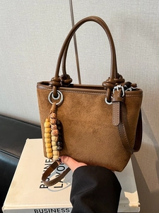 Brown suede bucket bag with round handles and wooden bead charm in a retro style