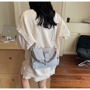 Vue détaillée d'un sac bandoulière gris en nylon avec boucles décoratives et zips latéraux