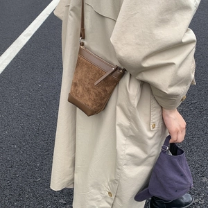 Detail of a brown matte suede bucket bag showing leather stitching and silver zipper