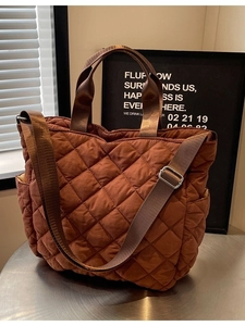 Quilted caramel tote bag with double handles and shoulder strap on a metal table