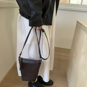 Detail of dark brown matte bucket bag with silver zipper and slim leather strap