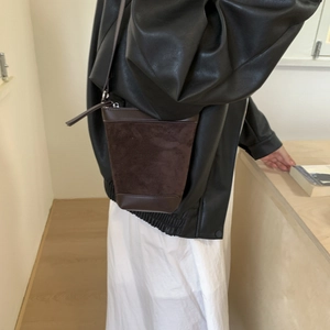 Detail of dark brown matte suede bucket bag with smooth leather trim and silver zipper