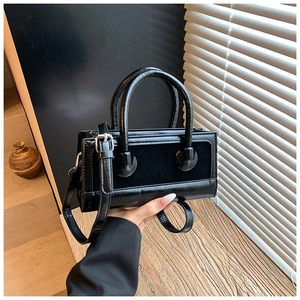 Detail of black rectangular handbag featuring mixed textures and round dual handles