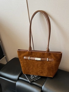 Brown minimalist suede tote bag with metal buckle on a black leather bench