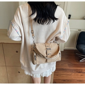 Détail du sac bandoulière en toile kaki avec boucle métallique et poches zippées