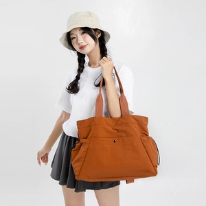 Close-up of a large orange nylon tote bag showing drawstring details and metal buckle