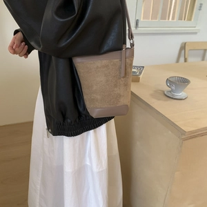 Detail of minimalist khaki suede bucket bag worn by model in a cozy cafe setting