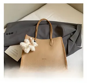 Detail of khaki tote bag with pebbled leather texture and plush bear charm on a suit