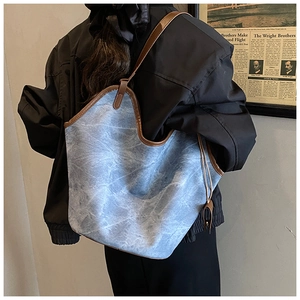 Detail of blue textured tote bag with brown leather trim shown on model's shoulder