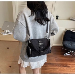 Détail du sac bandoulière en toile noire avec boucles argentées porté par une femme