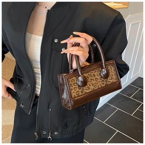 Detail of a brown leather small square bag with leopard print panel and round handles