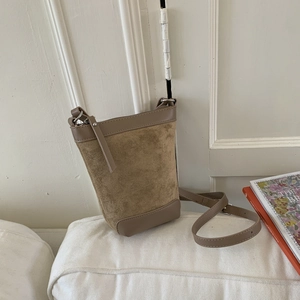 Detail view of khaki crossbody bucket bag with mixed leather texture on a white sofa