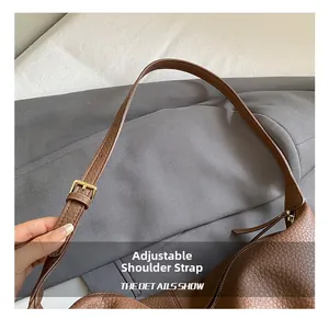 Detail of adjustable shoulder strap on brown pebble leather tote bag with gold buckle