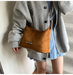 Detailed macro view of caramel suede dumpling bag featuring a silver fashion metal plaque