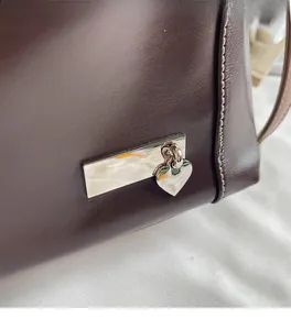 Détail du sac en cuir marron foncé avec plaque en métal argenté et breloque cœur