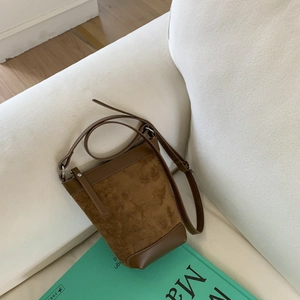 Detail of brown suede bucket bag with leather patchwork on a cozy cream sofa