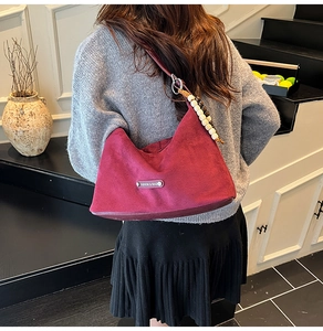 Detail view of burgundy faux suede half-moon bag with wooden bead and branded tag