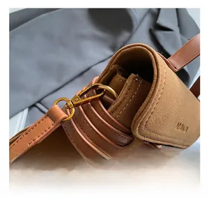 Detailed close-up of retro gold metal hook and precision stitching on a brown suede bag