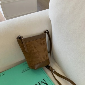 Close-up of brown suede bucket bag featuring leather trim on a white fabric sofa