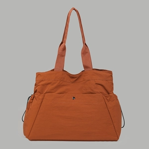 Detail of water-resistant orange nylon tote bag showing front snap pocket and side drawstrings