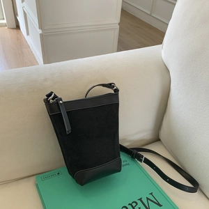 Detail of a black textured bucket bag showing the zipper and leather strap on a sofa